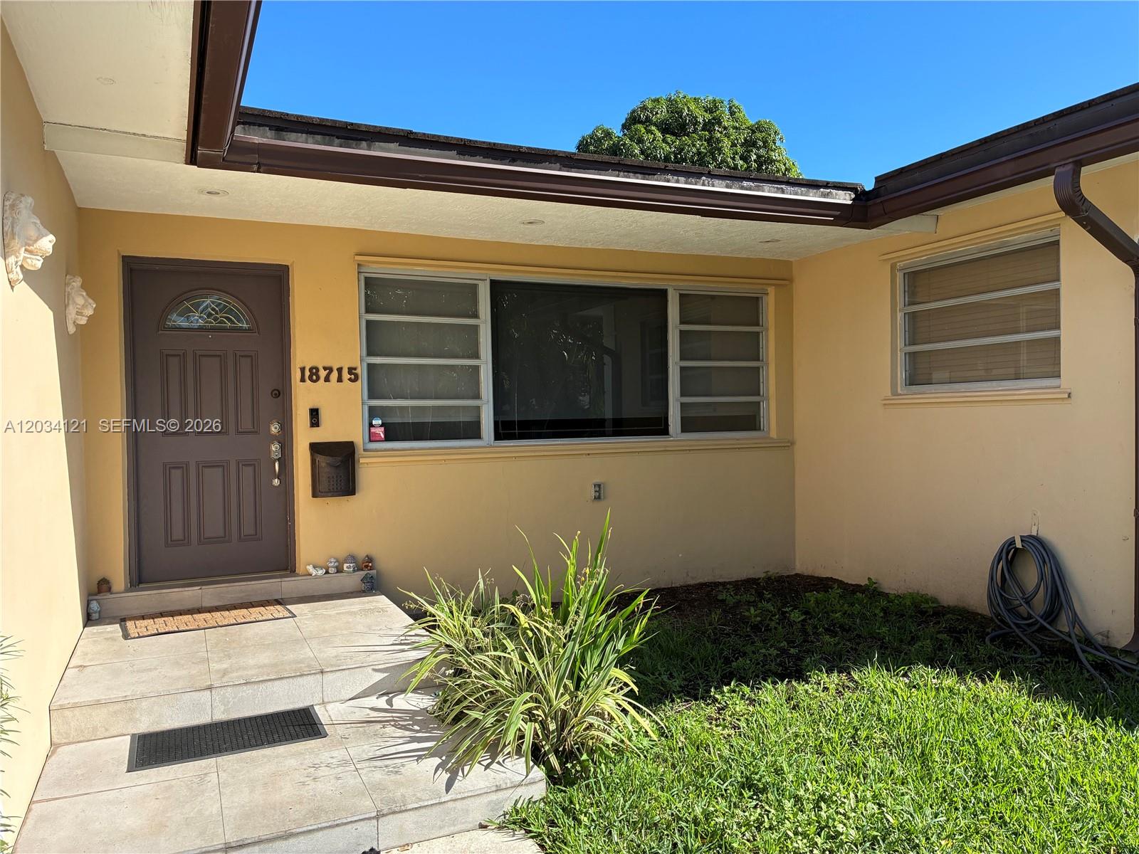 The exterior entrance features a dark blue front door, a window, and tiled steps — 18715 NE 18th Ave, Miami FL 33179, MIAMI, FL