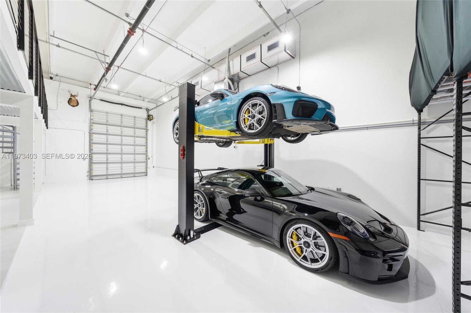 A high-ceiling garage features a two-post car lift stacking a blue and black Porsche — 13500 SW 134th Ave # 4A, Miami FL 33186, MIAMI, FL