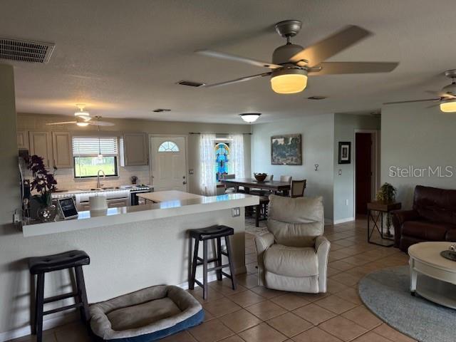 An open-concept kitchen and living area features a breakfast bar, ceiling fans, and tile flooring — 5015 TWIN LAKES LANE, BARTOW, FL