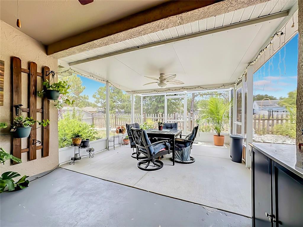 A screened-in patio features a dining set, ceiling fan, and potted plants on concrete flooring — 6630 CAMBRIDGE PARK DRIVE, APOLLO BEACH, FL