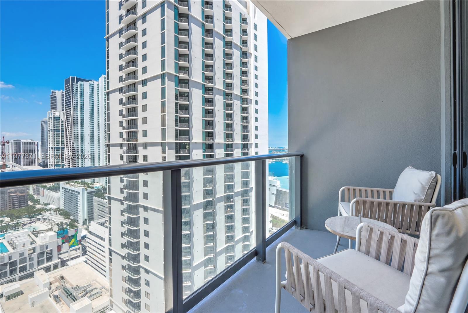 A high-rise balcony features two chairs, a small table, and views of surrounding city skyscrapers — 159 NE 6th St # 2711, Miami FL 33132, MIAMI, FL