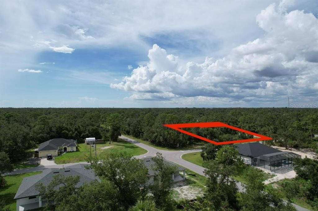 An aerial view shows a vacant, wooded lot outlined in red near suburban houses — 1243 MILIKEN TERRACE, PORT CHARLOTTE, FL