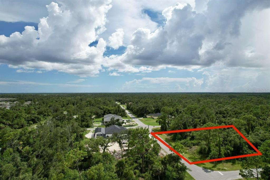 An aerial view shows a vacant, wooded residential lot outlined in red along a paved road — 1243 MILIKEN TERRACE, PORT CHARLOTTE, FL