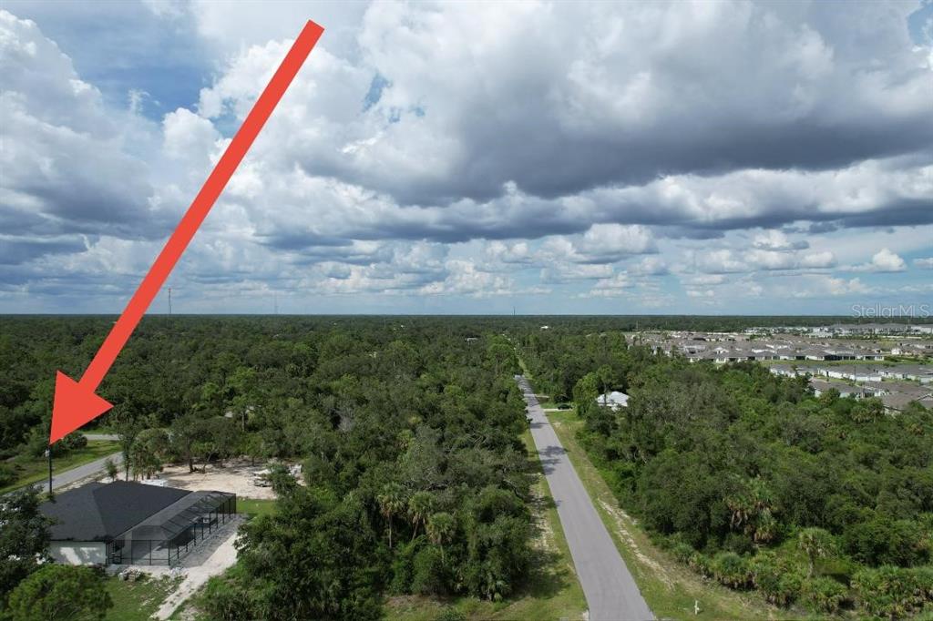 An aerial view shows a house with a screened pool enclosure near a wooded road — 1243 MILIKEN TERRACE, PORT CHARLOTTE, FL