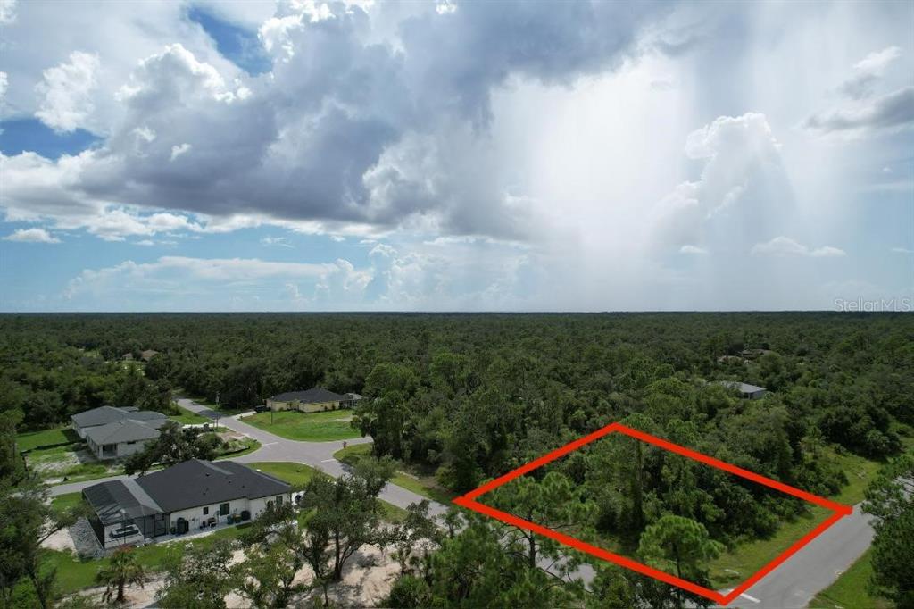An aerial view shows a vacant, wooded residential lot outlined in red near paved roads — 1243 MILIKEN TERRACE, PORT CHARLOTTE, FL