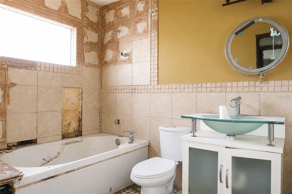 A bathroom in need of renovation with a bathtub, toilet, and glass vessel sink vanity — 419 ALLSPICE COURT, KISSIMMEE, FL