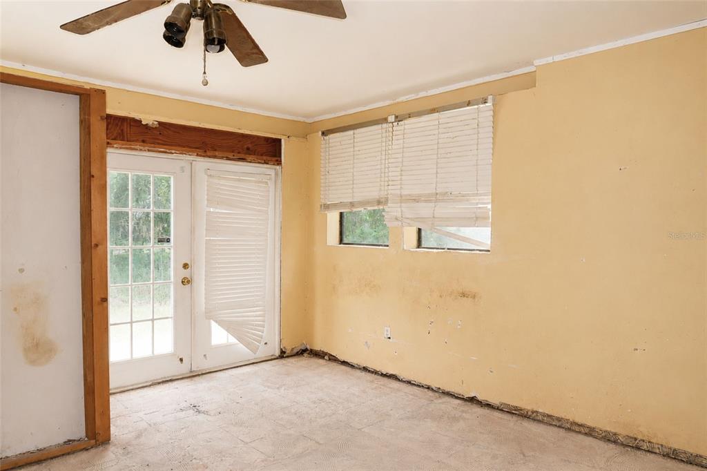 An unfinished room with yellow walls, a ceiling fan, French doors, and bare concrete floors — 419 ALLSPICE COURT, KISSIMMEE, FL