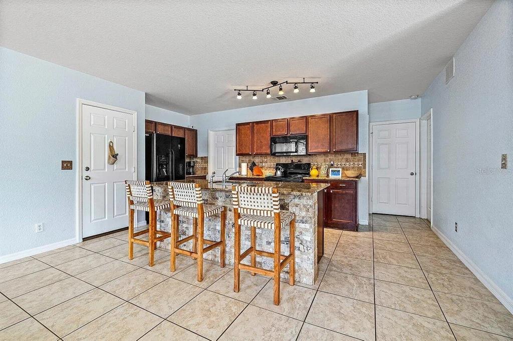 A kitchen features dark wood cabinets, granite countertops, a stone-faced island, and three bar stools — 119 SW 2ND AVENUE, BOYNTON BEACH, FL