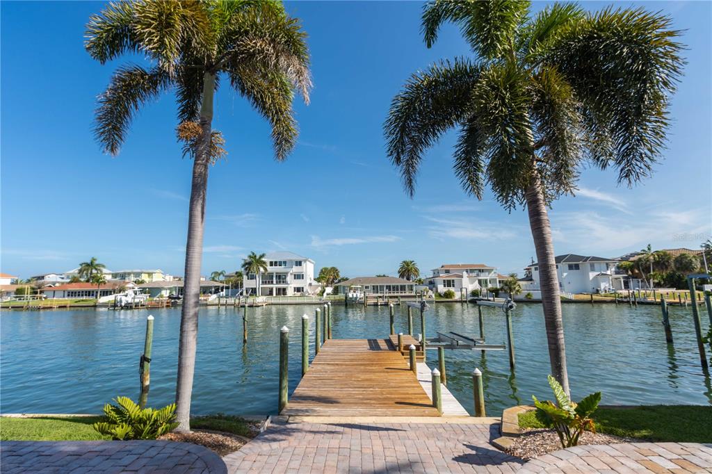 A wooden dock extends into a canal lined with palm trees and waterfront houses — 440 PALM ISLAND SE, CLEARWATER BEACH, FL