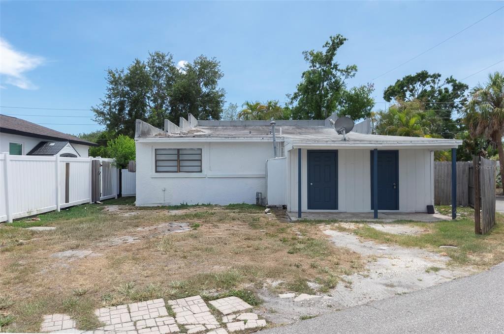 A single-story white house with a flat roof, two blue doors, and a dirt yard — 3651 HAINES ROAD N, ST PETERSBURG, FL