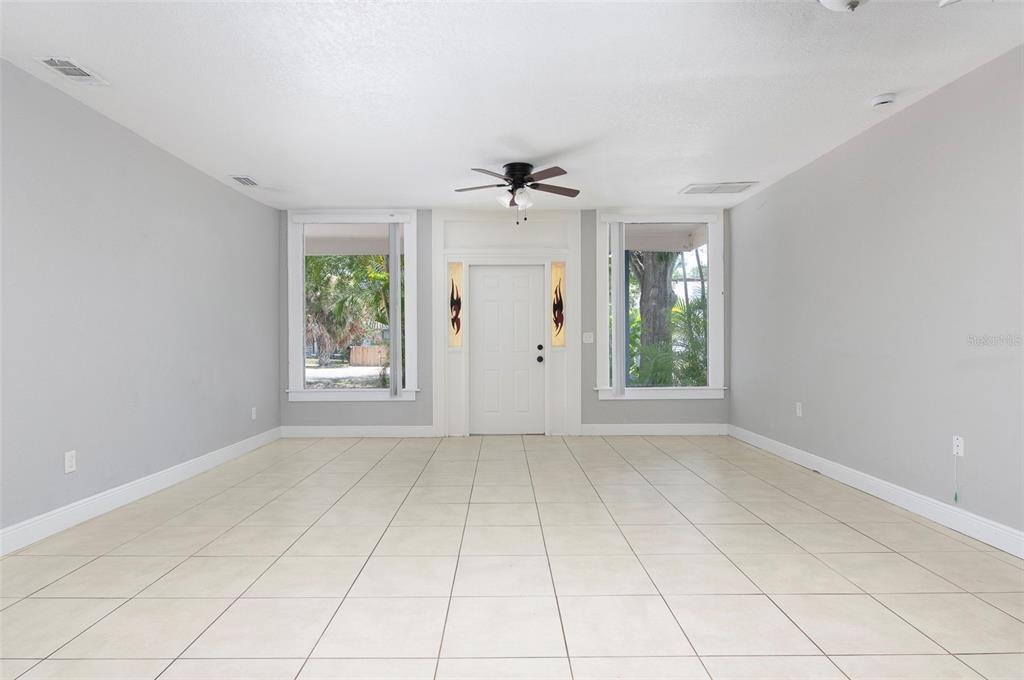 An empty room with light-colored tile flooring, gray walls, a ceiling fan, and a front door — 3651 HAINES ROAD N, ST PETERSBURG, FL