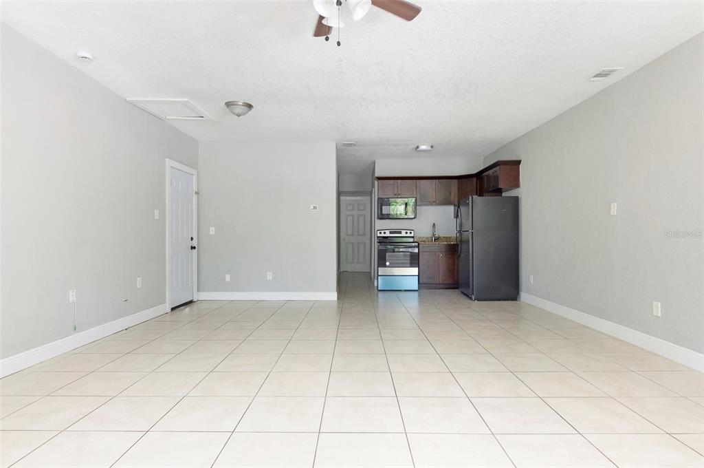 An open-concept room features light-colored tile flooring, gray walls, and a small kitchen area — 3651 HAINES ROAD N, ST PETERSBURG, FL
