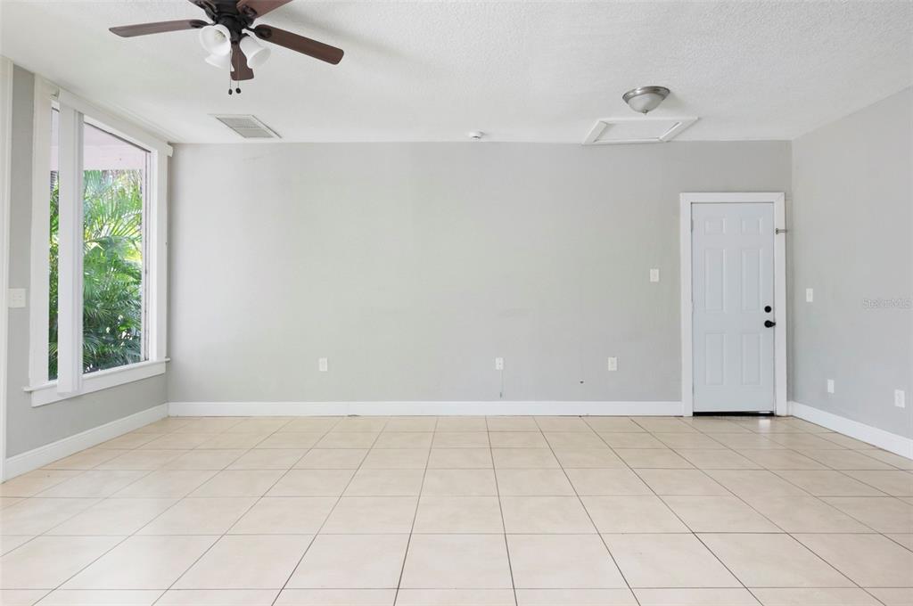 An empty room with light gray walls, beige tile flooring, a ceiling fan, and a door — 3651 HAINES ROAD N, ST PETERSBURG, FL