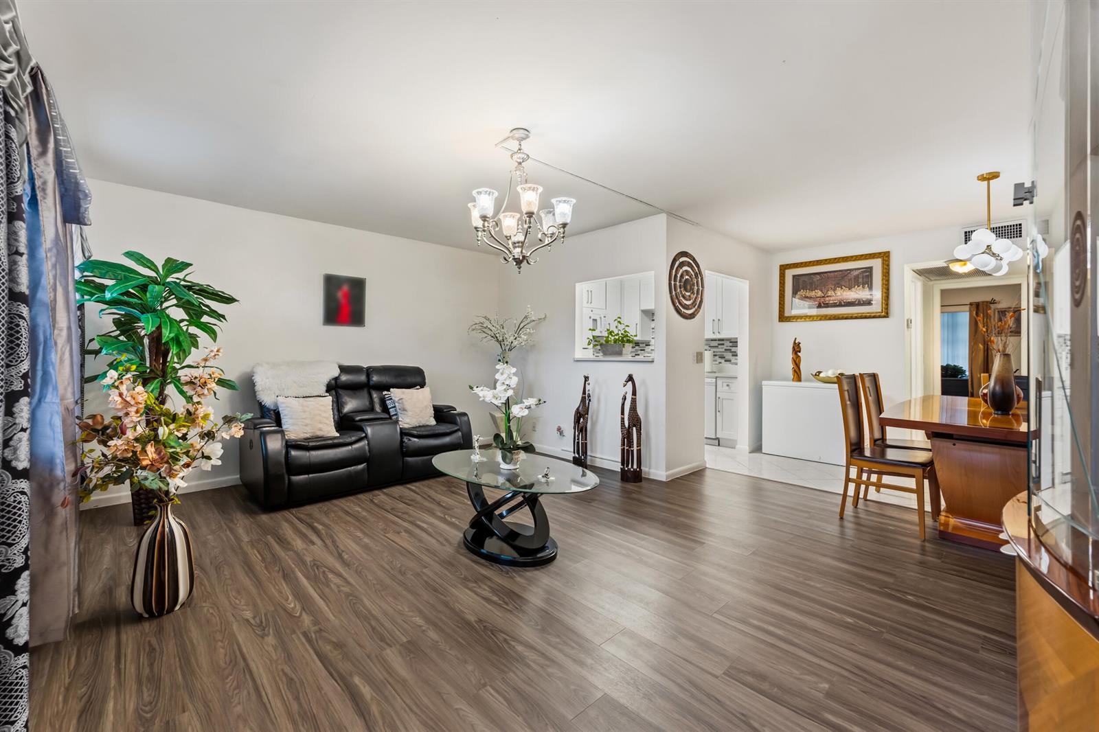 A living and dining area features wood-look flooring, a black leather loveseat, and a chandelier — 126 Southampton B, West Palm Beach FL 33417, WEST PALM BEACH, FL