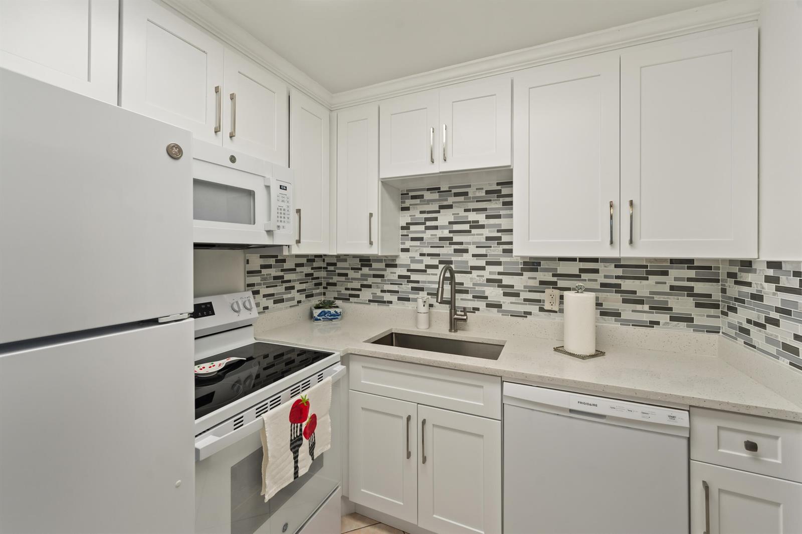 A kitchen features white cabinets, a mosaic tile backsplash, stainless steel appliances, and quartz countertops — 126 Southampton B, West Palm Beach FL 33417, WEST PALM BEACH, FL