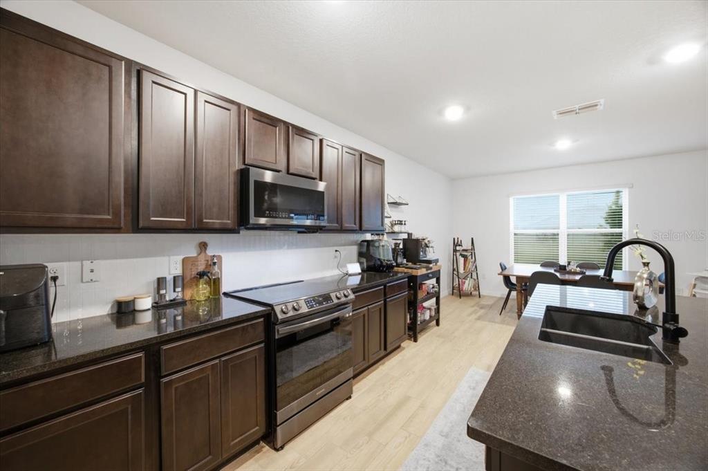 A kitchen with dark wood cabinets, granite countertops, stainless steel appliances, and a center island — 325 AUBURN GROVE CROSSING, AUBURNDALE, FL