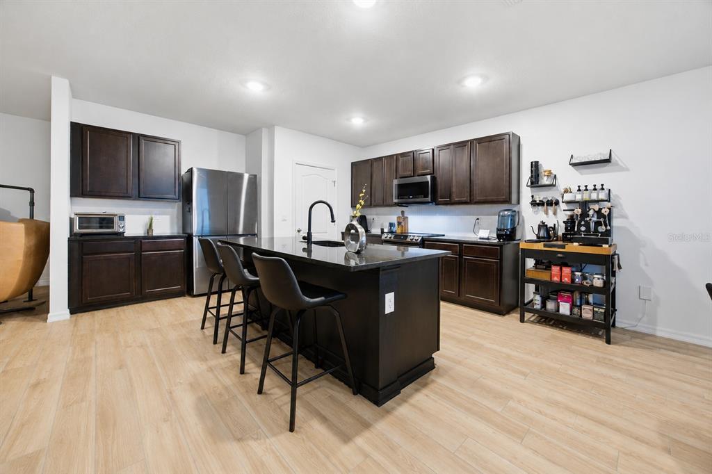 A modern kitchen features dark wood cabinets, a black island with bar seating, and light flooring — 325 AUBURN GROVE CROSSING, AUBURNDALE, FL