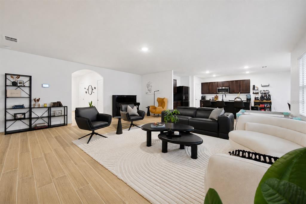 An open-concept living room features light wood-look tile flooring, a large area rug, and dark furniture — 325 AUBURN GROVE CROSSING, AUBURNDALE, FL