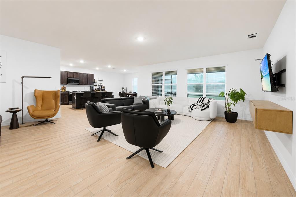 An open-concept living room features light wood-look flooring, modern furniture, and an adjacent kitchen — 325 AUBURN GROVE CROSSING, AUBURNDALE, FL