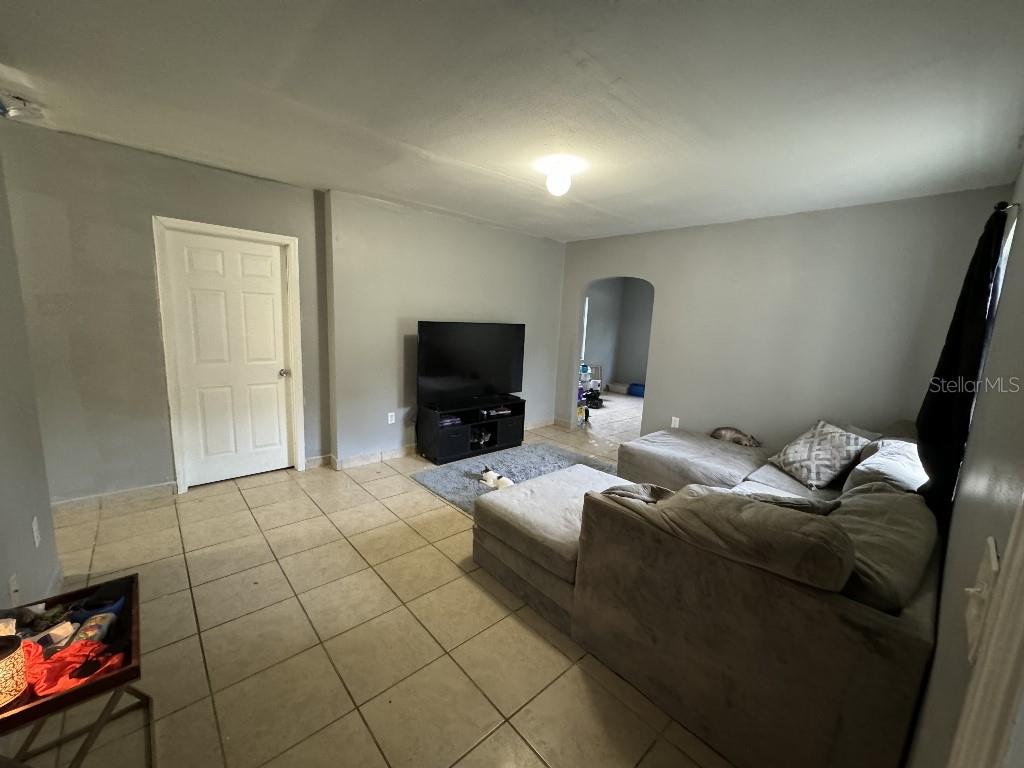 A living room with gray walls, tile flooring, a sectional sofa, and a television console — 419 AVENUE M NE, WINTER HAVEN, FL