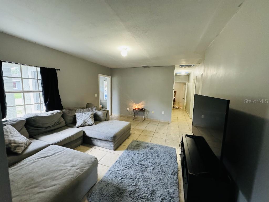 A living room features a large gray sectional sofa, a television, and tile flooring — 419 AVENUE M NE, WINTER HAVEN, FL