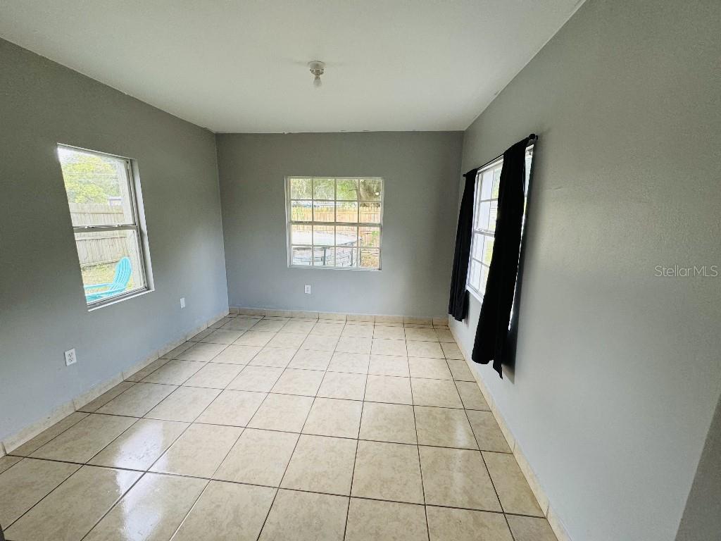 An empty room with light gray walls, beige tile flooring, and three windows — 419 AVENUE M NE, WINTER HAVEN, FL