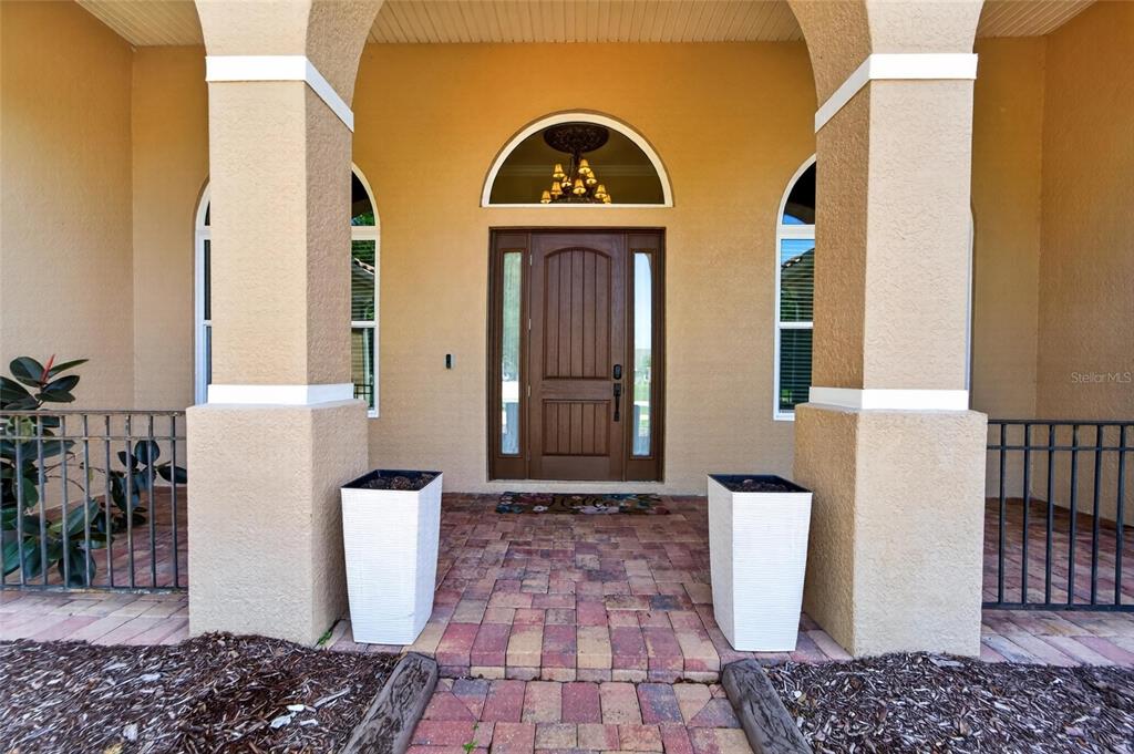 A front entryway features a wooden door, arched transom window, and two white planters — 5207 LAKE VENICE DRIVE, WIMAUMA, FL