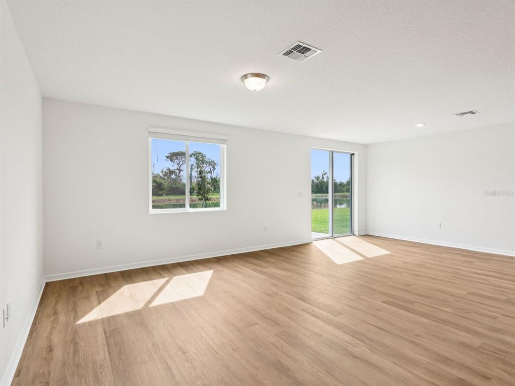 An empty room with light wood-look flooring, white walls, a window, and sliding glass doors — 7717 SATTERFIELD TERRACE, PARRISH, FL