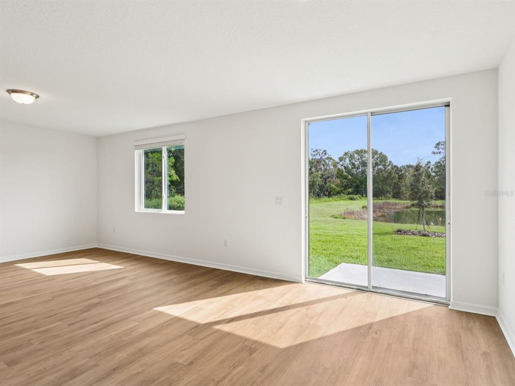 An empty room with light wood-look flooring, a window, and sliding glass doors to a yard — 7717 SATTERFIELD TERRACE, PARRISH, FL