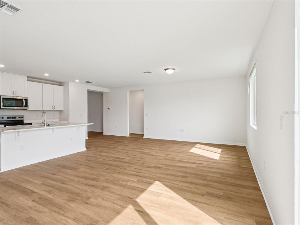 An open-concept kitchen and living area featuring white cabinets, stainless steel appliances, and wood-look flooring — 7717 SATTERFIELD TERRACE, PARRISH, FL