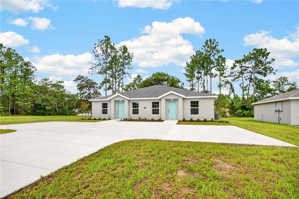 A single-story duplex with light gray stucco walls, two teal doors, and a large concrete driveway — 14001 SW 60TH TERRACE, OCALA, FL