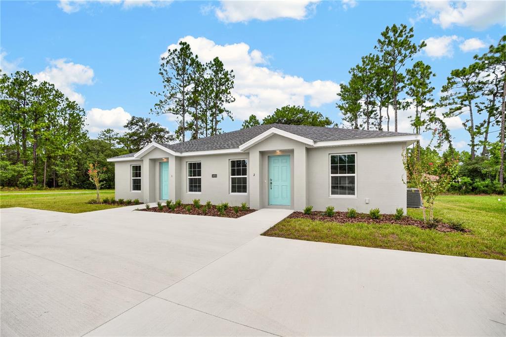 A single-story duplex with light gray stucco walls, two light blue doors, and a concrete driveway — 14001 SW 60TH TERRACE, OCALA, FL