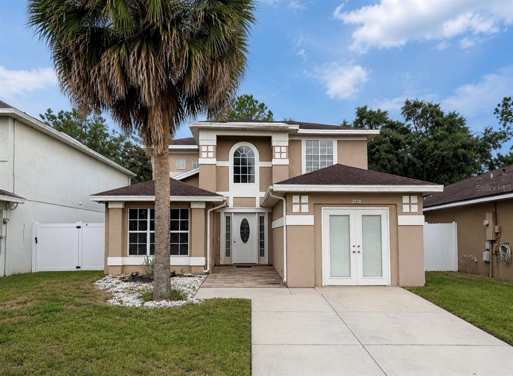 A two-story tan stucco house features a palm tree, a paved driveway, and a garage — 2728 EMERSON LANE, KISSIMMEE, FL