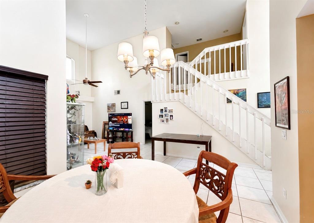 A dining area with a round table and chairs sits before a staircase and living room — 2728 EMERSON LANE, KISSIMMEE, FL