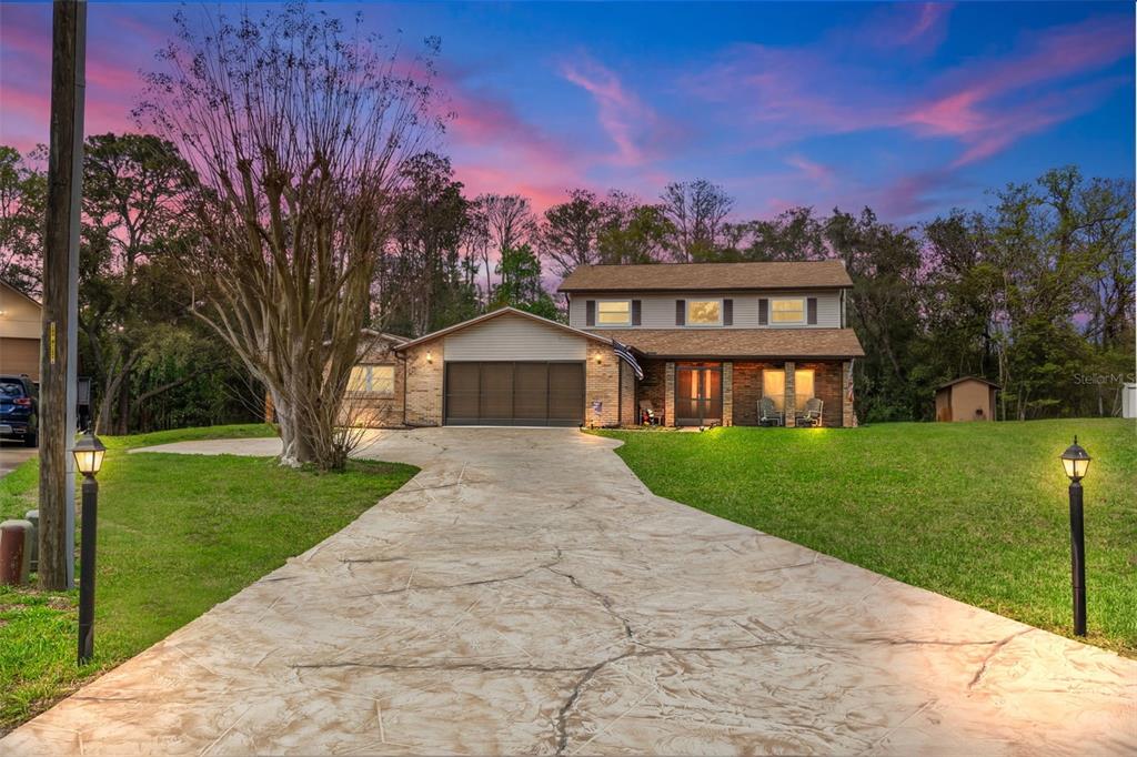 A two-story brick house with a large driveway and a sunset sky in the background — 1357 DINSMORE COURT, NEW PORT RICHEY, FL