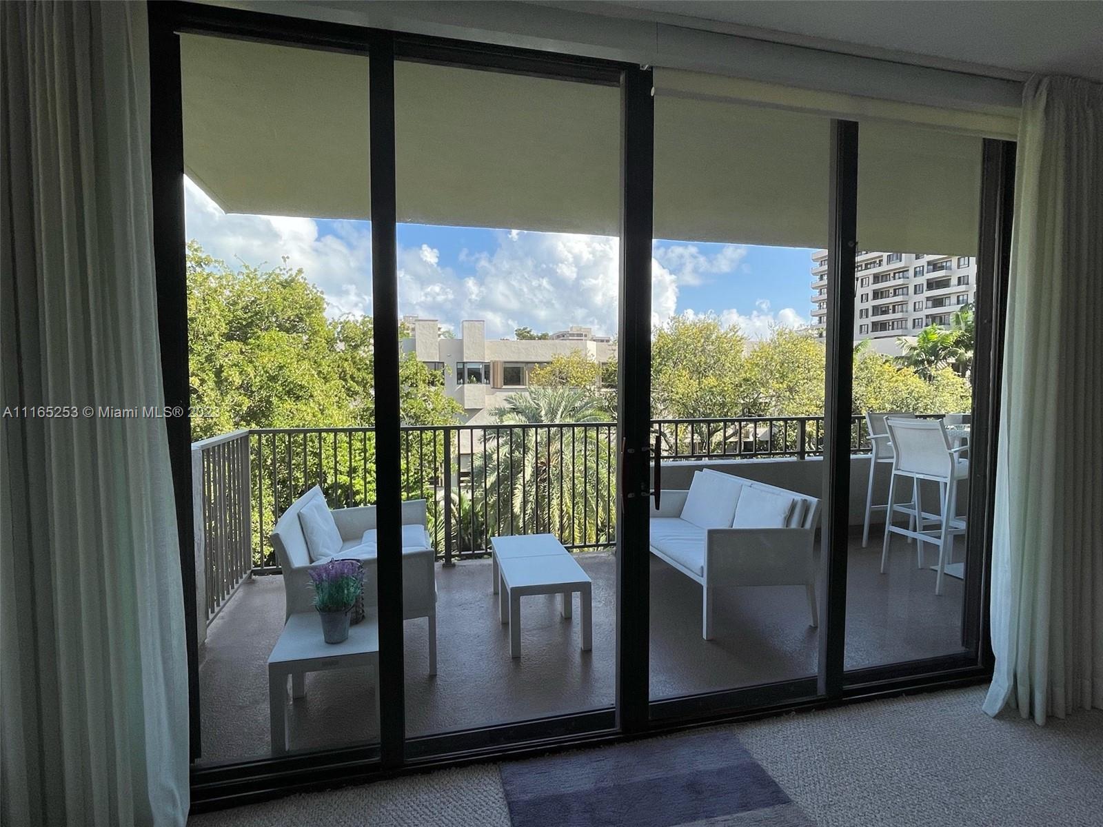 A balcony with white patio furniture is viewed through large sliding glass doors — 101 Crandon Blvd # 473, Key Biscayne FL 33149, KEY BISCAYNE, FL