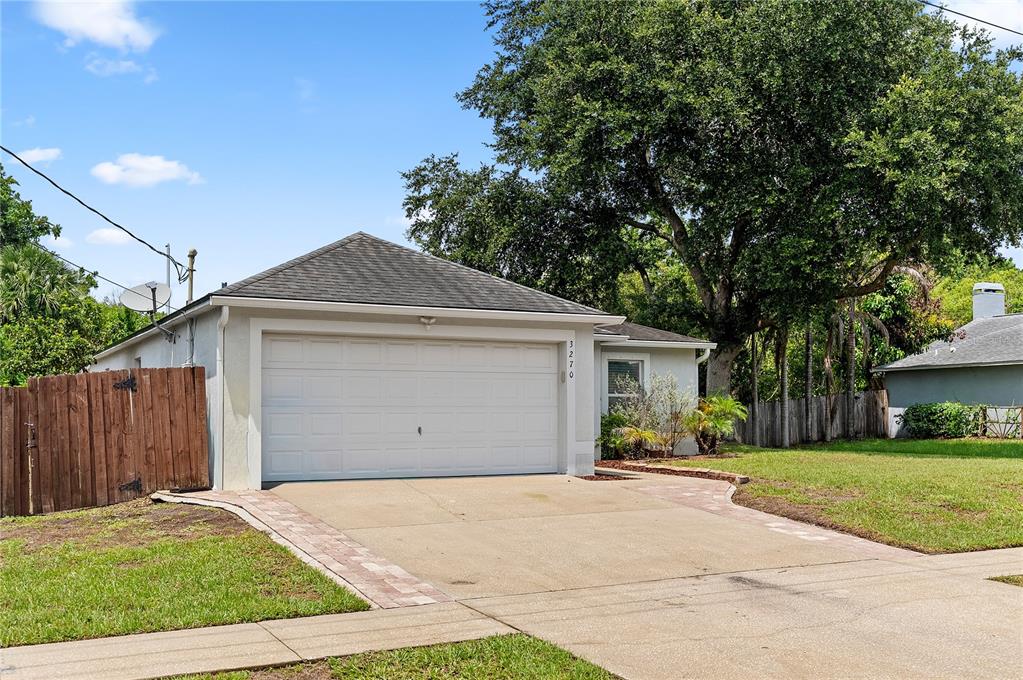 A single-story house with a white garage door, a concrete driveway, and a large tree — 3270 CRAGGY BLUFF PLACE, COCOA, FL