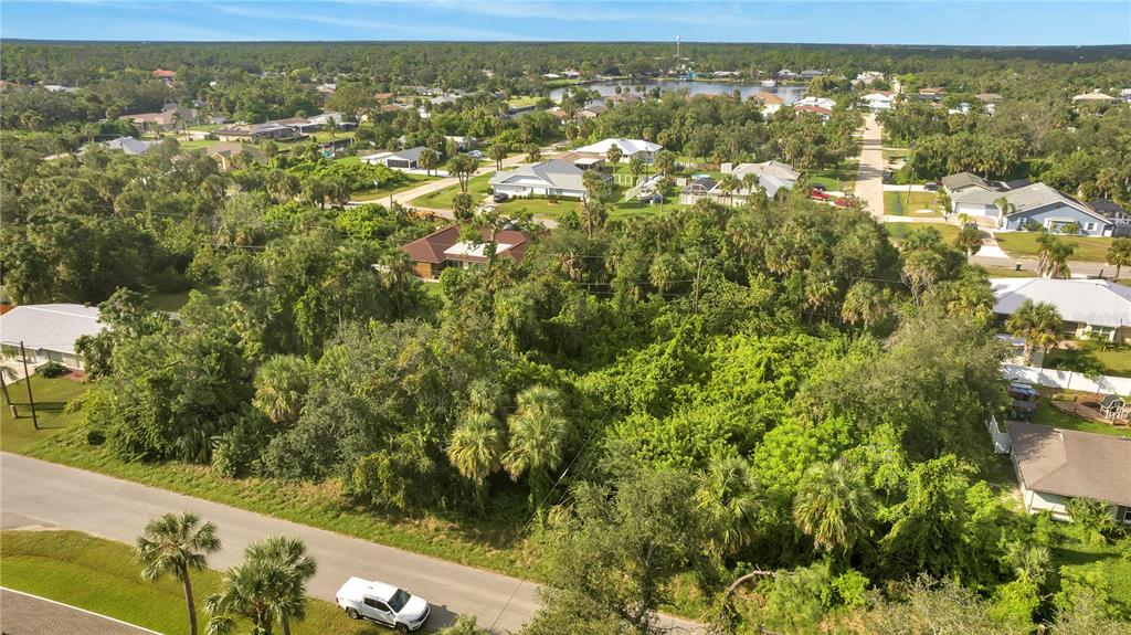 An aerial view shows a vacant, tree-covered residential lot situated between suburban houses and streets — 18444 ACKERMAN AVENUE, PORT CHARLOTTE, FL