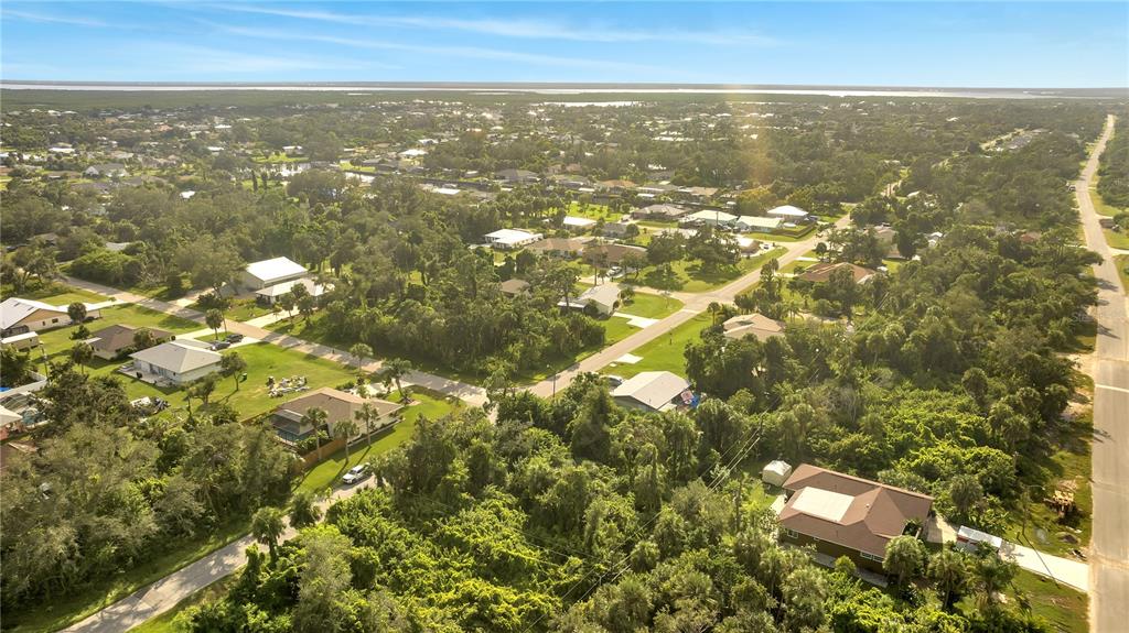 An aerial view shows a suburban neighborhood with houses, dense trees, and paved roads — 18444 ACKERMAN AVENUE, PORT CHARLOTTE, FL