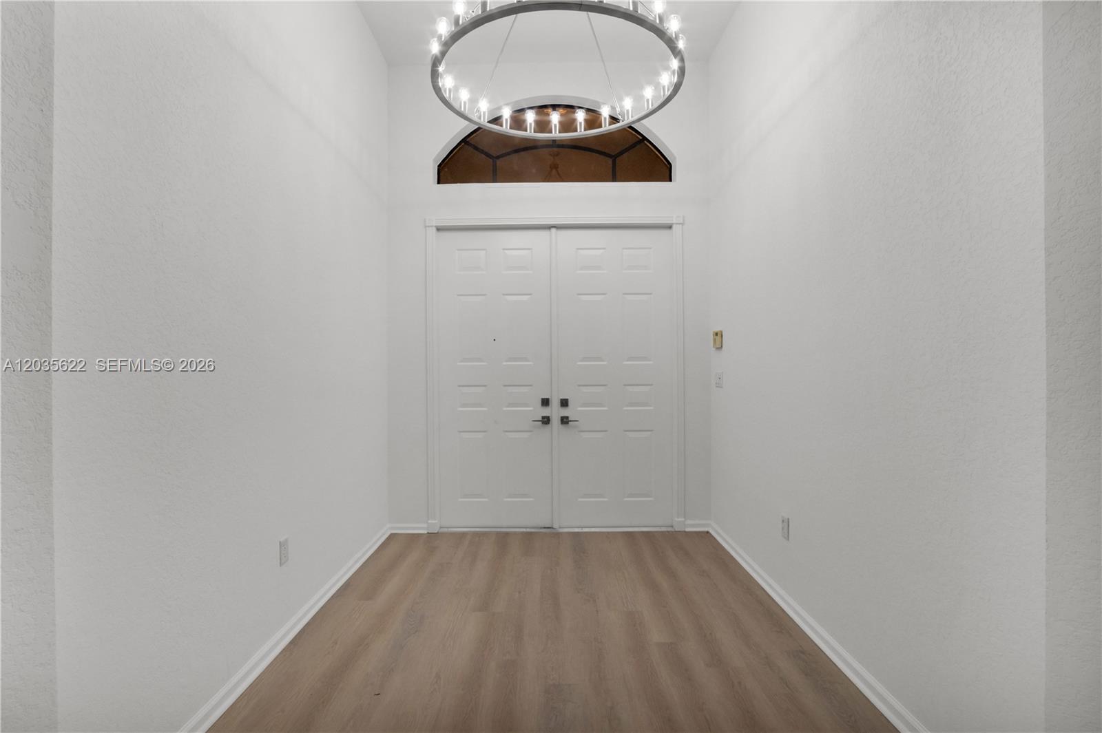 A bright entryway features white walls, light wood-look flooring, double doors, and a circular chandelier — 7747 Via Grande, Boynton Beach FL 33437, BOYNTON BEACH, FL