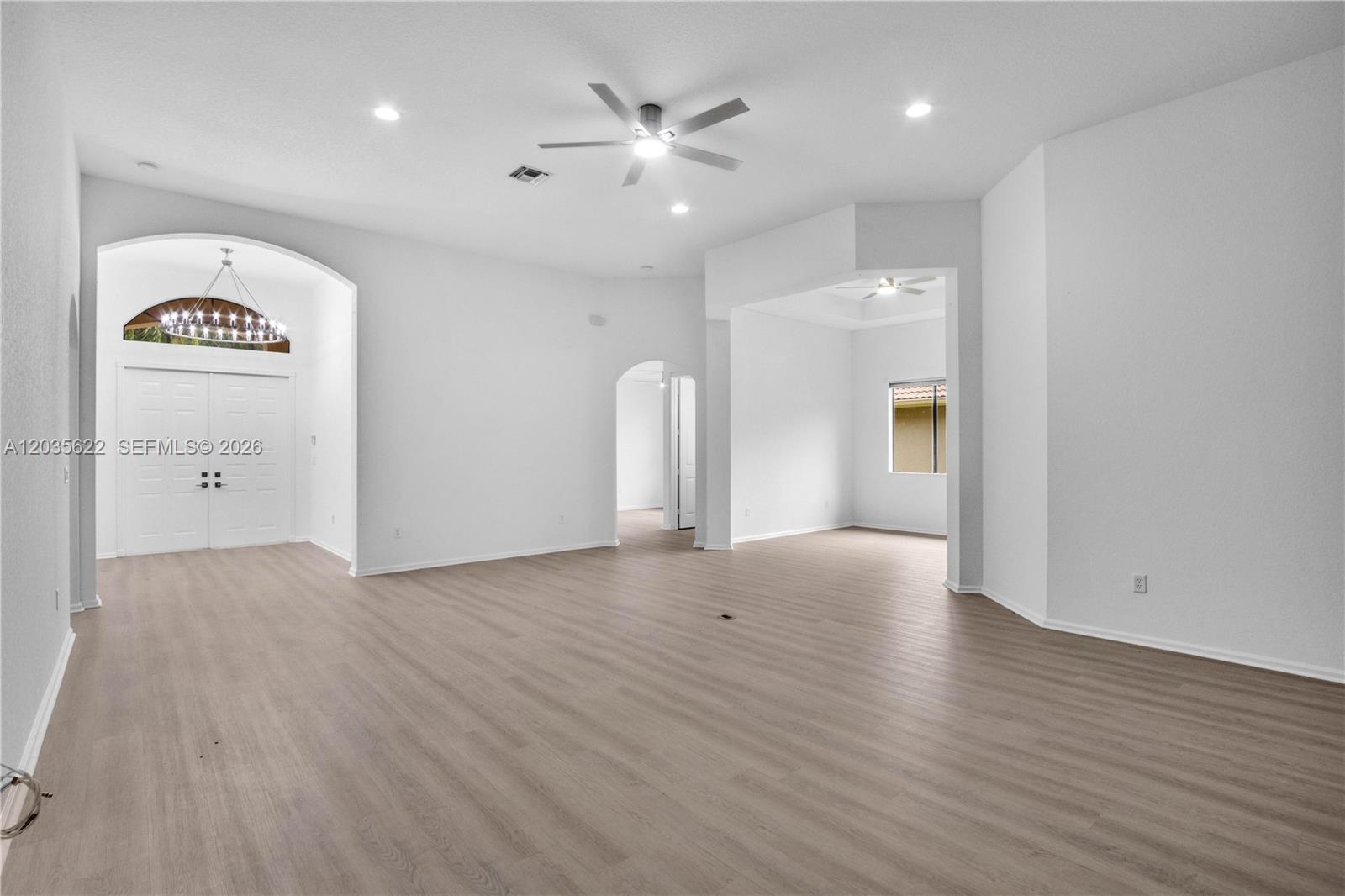 A spacious, empty living area features light-colored wood-look flooring, white walls, and a ceiling fan — 7747 Via Grande, Boynton Beach FL 33437, BOYNTON BEACH, FL