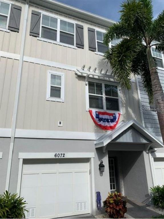 A three-story townhouse exterior with a garage, light siding, and a patriotic bunting decoration — 6072 MOORINGS DRIVE S, ST PETERSBURG, FL