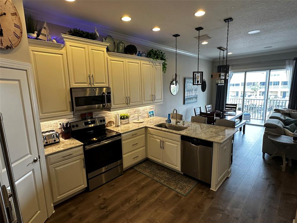 A kitchen features white cabinetry, granite countertops, stainless steel appliances, and wood-look flooring — 6072 MOORINGS DRIVE S, ST PETERSBURG, FL