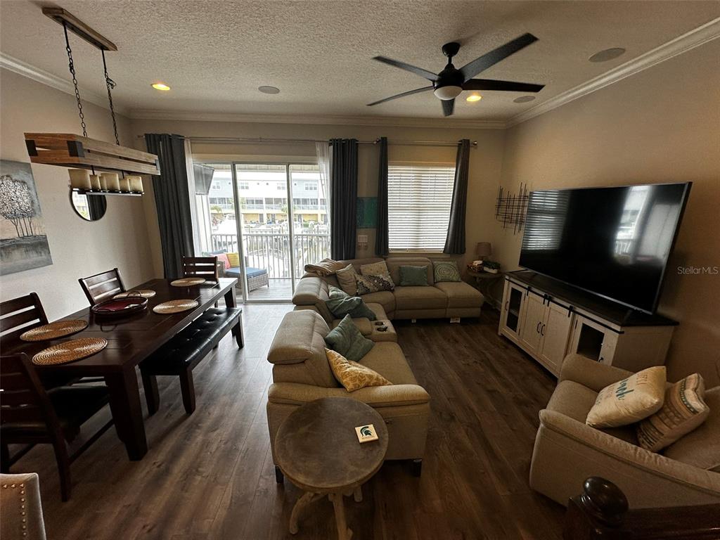 This open-concept living and dining area features wood flooring, a sectional sofa, and balcony access — 6072 MOORINGS DRIVE S, ST PETERSBURG, FL