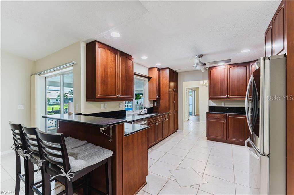 A kitchen features dark wood cabinets, black countertops, a breakfast bar, and light tile flooring — 3319 SE 17TH AVENUE, CAPE CORAL, FL
