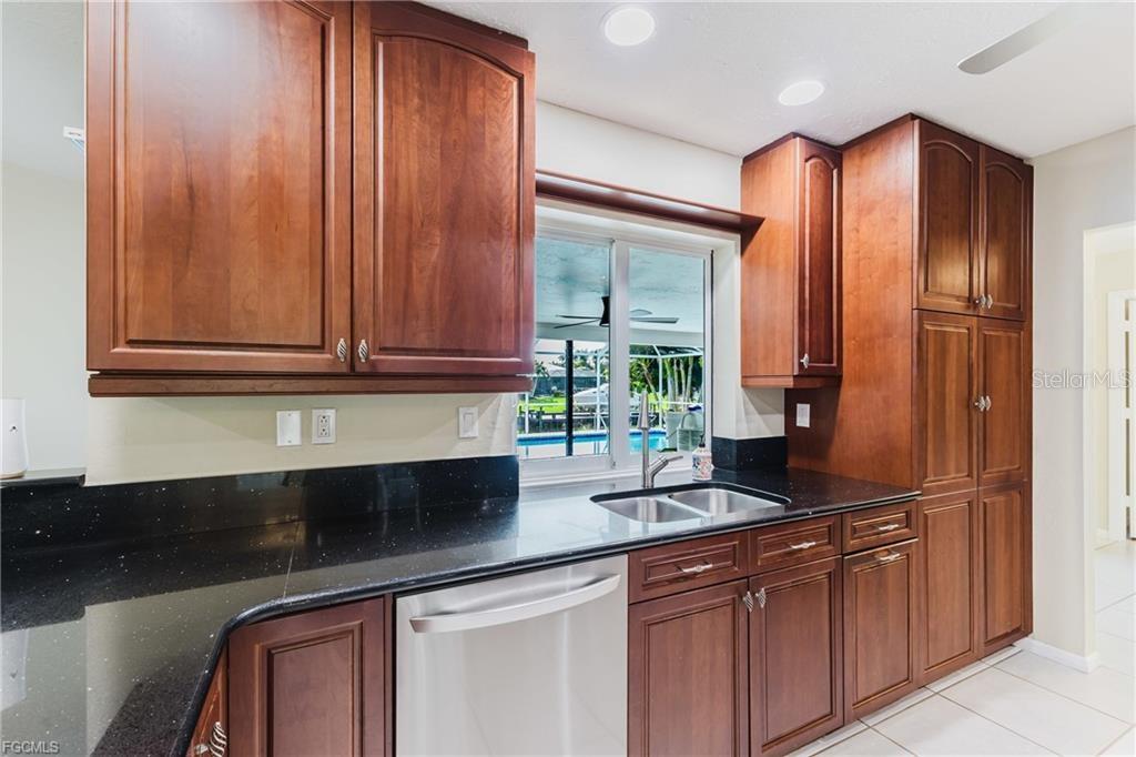 A kitchen features dark wood cabinets, black countertops, a stainless steel dishwasher, and a window — 3319 SE 17TH AVENUE, CAPE CORAL, FL