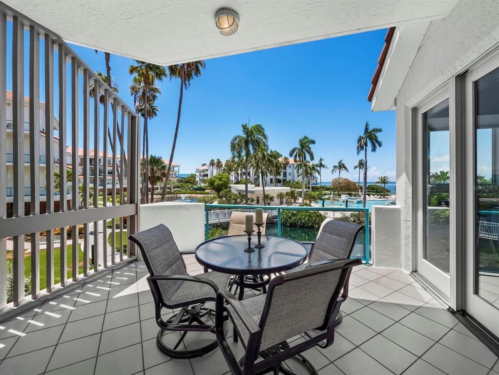 A balcony with a glass-topped table and four chairs overlooks a pool and palm trees — 350 GULF OF MEXICO DRIVE UNIT 213, LONGBOAT KEY, FL