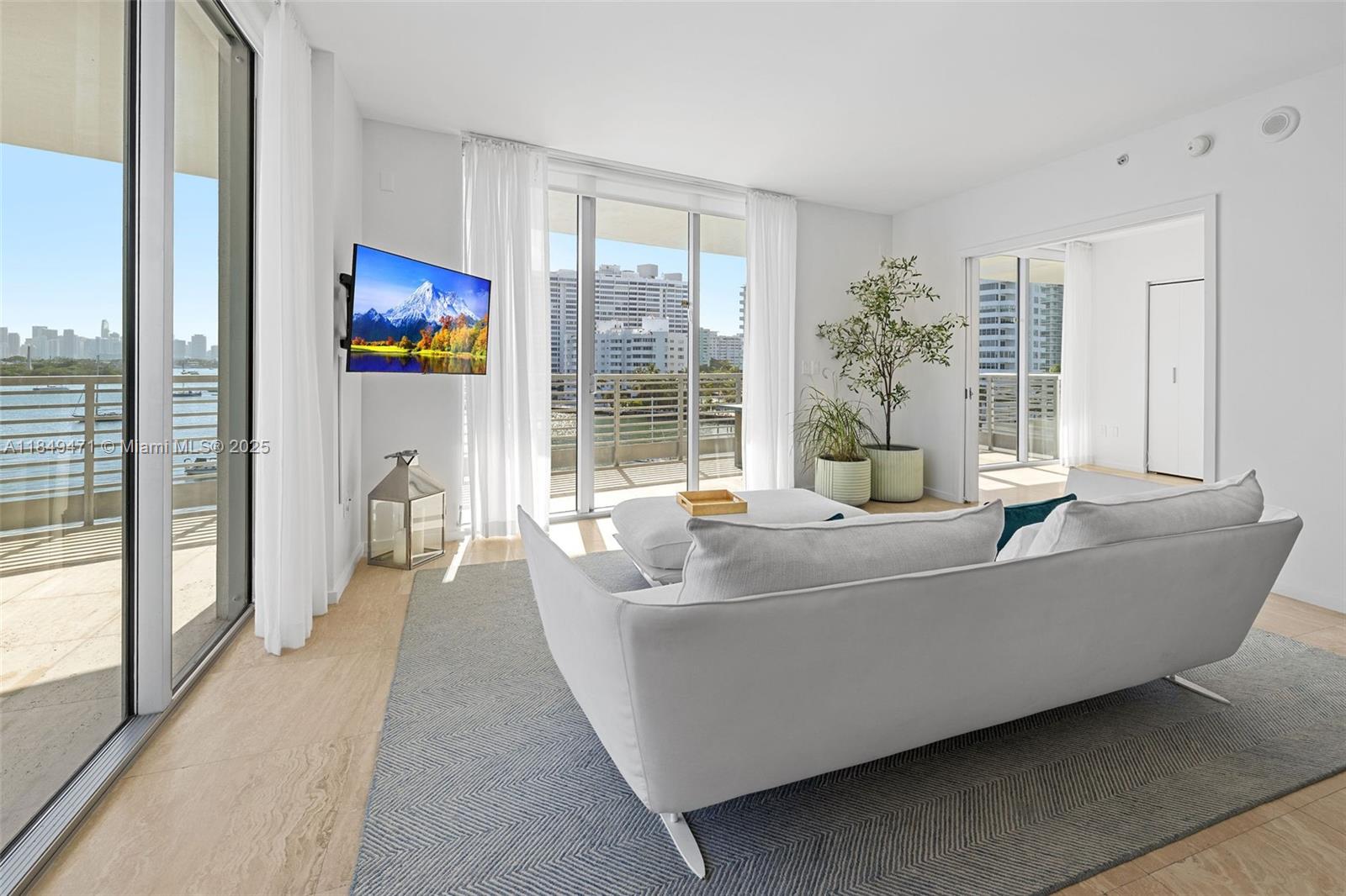 A bright living room features a white sofa, a wall-mounted television, and floor-to-ceiling balcony doors — 1445 16th St # 602, Miami Beach FL 33139, MIAMI BEACH, FL