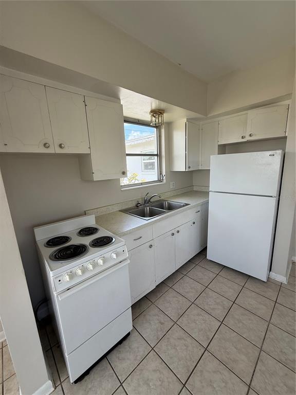 A kitchen features white cabinets, a white electric stove, a refrigerator, and tiled flooring — 698 UNION STREET, DUNEDIN, FL