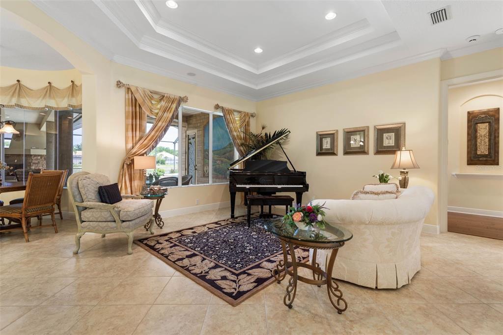 A living room with a grand piano, tile flooring, a tray ceiling, and neutral walls — 57 OSPREY CIRCLE, PALM COAST, FL